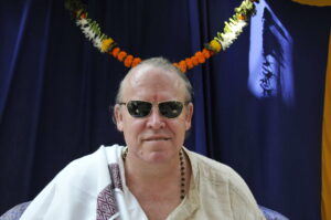 Medition Master Mark Griffin seated with sun glasses against blue background.