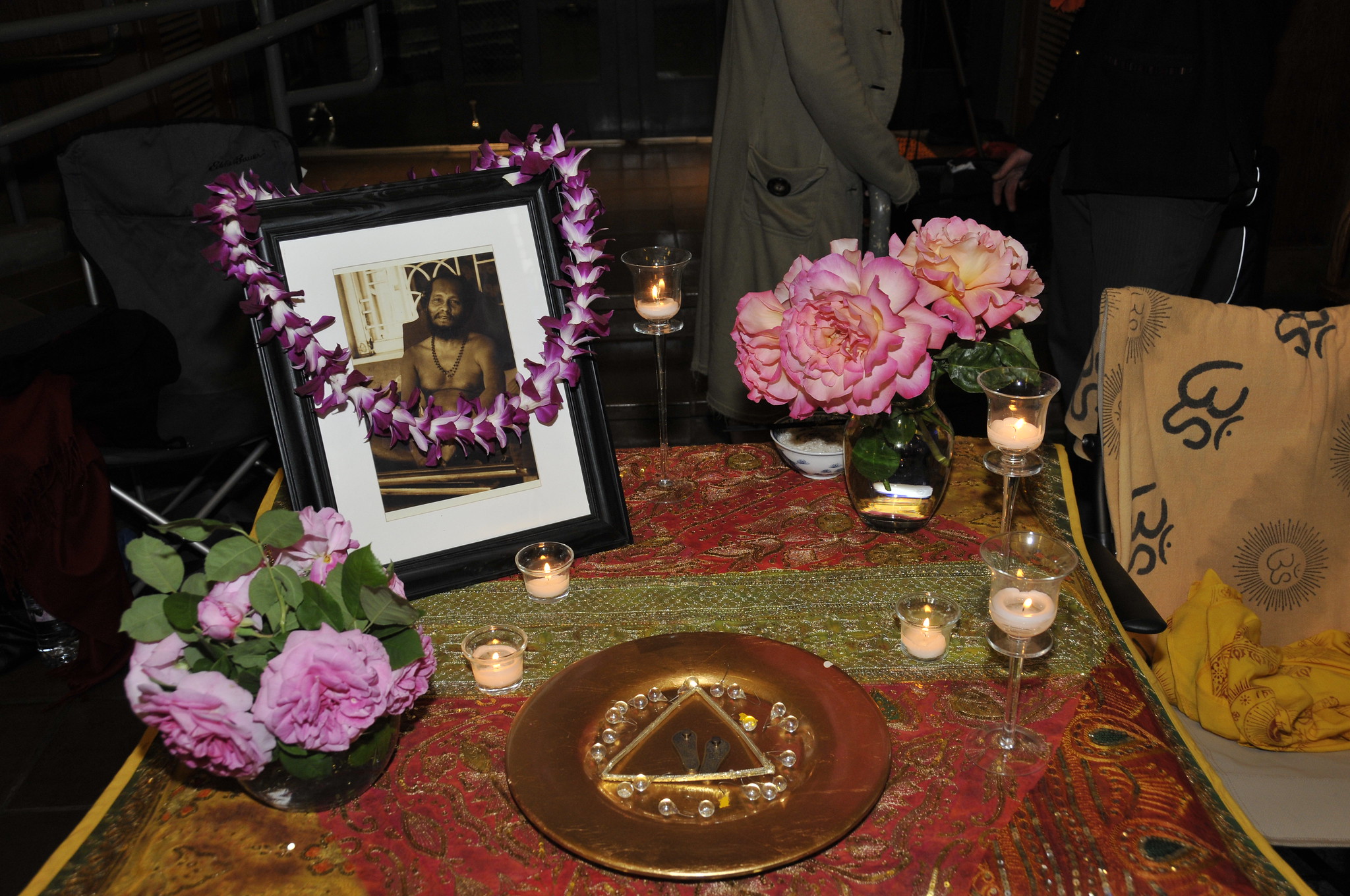 Puja table with flowers and photo of Swami Muktananda seated and smiling.